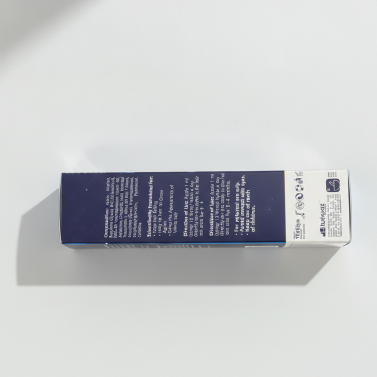 A rectangular product box shown from above on a white surface, with the dark blue side displaying dense white text and the white end cap showing a barcode and product name.